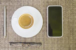 bovenaanzicht van koffie met penglazen en mobiele telefoon over geweven bamboeachtergrond foto