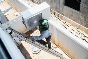 man installeert muurcompressor van airconditioner tijdens het warme seizoen foto