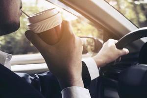 man rijdt auto terwijl hij een kopje koffie vasthoudt foto