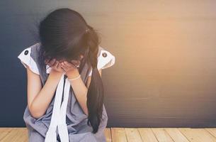 verdrietig Aziatisch meisje zittend op een witte houten vloer foto