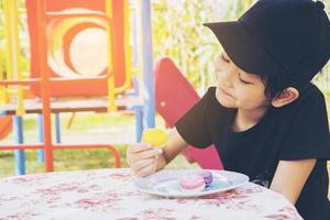 Aziatische jongen die macaron eet met speelplaatsachtergrond foto