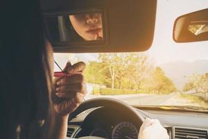 vrouw die haar gezicht opmaakt met lippenstift tijdens het autorijden, onveilig gedrag foto