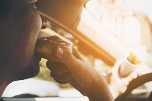 man die donuts en chips eet tijdens het autorijden - multitasking onveilig rijconcept foto