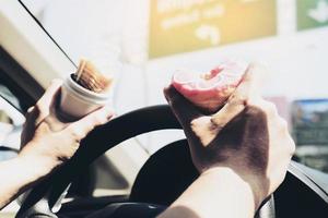 man die donuts en chips eet tijdens het autorijden - multitasking onveilig rijconcept foto