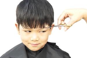 een jongen is zijn haar geknipt door een kapper die over witte achtergrond wordt geïsoleerd foto