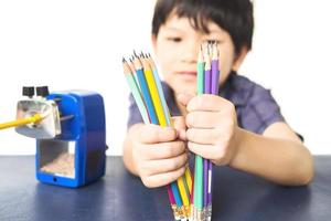 een jongen slijpt zijn potlood met een mechanische slijper op een witte achtergrond foto
