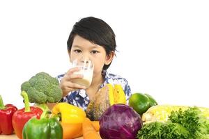 Aziatische gezonde jongen die gelukkige uitdrukking met een glas melk en verscheidenheids verse kleurrijke groente toont over witte achtergrond foto