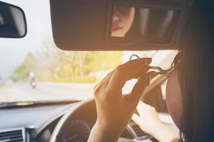 vrouw make-up haar gezicht met wimperkruller tijdens het autorijden, onveilig gedrag foto