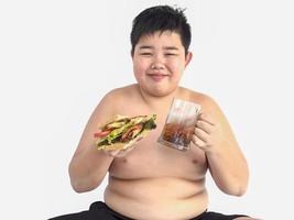 een dikke jongen eet vrolijk een broodje met frisdrank foto