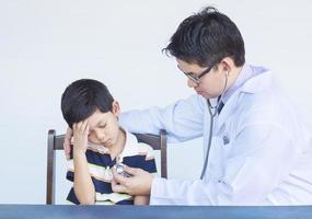 zieke aziatische jongen wordt onderzocht door een mannelijke arts op een witte achtergrond foto