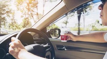 man die in de auto rijdt met één hand terwijl hij een koffiekopje in de andere hand houdt foto