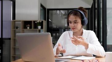 lachend meisje in koptelefoon zit aan bureau kijk naar laptopscherm studeer online, gelukkige slimme jonge vrouw in koptelefoon volgt webcursus of training op computer, concept voor onderwijs op afstand foto