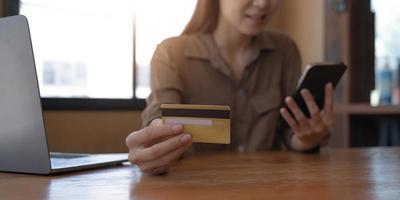 close-upbeeld van de hand van een vrouw die een creditcard vasthoudt en op een mobiele telefoon op een houten tafel in het kantoor drukt foto