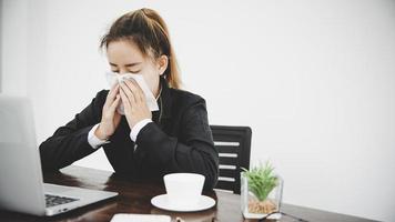 zieke jonge aziatische zakenvrouw die alleen op het werk zit niezen foto