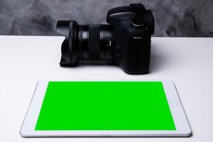 een zwarte digitale camera en een tablet met een leeg scherm op een tafel. foto
