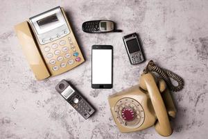 een oude telefoon met draaiknop, een vaste lijn, een verouderde mobiele telefoon en smartphone op een grunge-achtergrond. foto