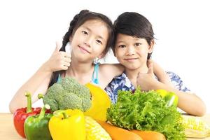 Aziatische jongen en meisje laten zien genieten van expressie met verse kleurrijke groenten geïsoleerd op witte achtergrond foto