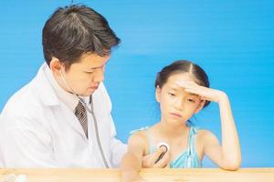 ziek Aziatisch meisje wordt behandeld door mannelijke arts over blauwe achtergrond foto