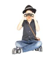 7 jaar oude Aziatische reizigersjongen zit en gebruikt een verrekijker geïsoleerd op een witte achtergrond foto