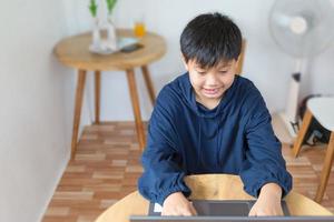lachende aziatische jongen die aan het chatten is met vrienden of een student die internet bestudeert op sociale netwerken die thuis voor de laptop zit. chatten op sociale media en videoconferenties. foto