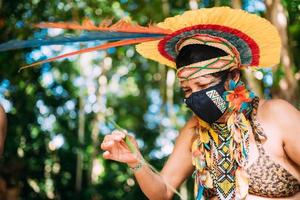 indiaan van de pataxo-stam met een veren hoofdtooi en beschermend masker tegen de covid-19 pandemie. inheemse vrouw uit brazilië die ambachten maakt foto