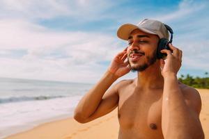 zomervakantie, technologie en internet concept. Latijns-Amerikaanse man luistert muziek met koptelefoon en zonnet op het strand foto