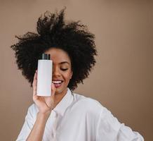 schoonheid latijnse vrouw met afro kapsel. Braziliaanse vrouw. met lege shampooverpakking. gekruld haar. kapsel. pastelkleurige achtergrond. foto