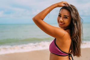 mooie jonge Latijns-Amerikaanse vrouw op het strand. vrouw zittend op het strandzand kijkend naar de camera op een mooie zomerdag foto