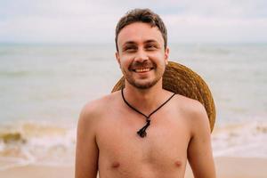 jonge Latijns-Amerikaanse man op het strand met een hoed. glimlachende man die naar links kijkt foto