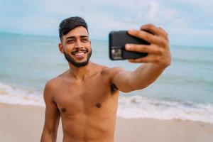 gelukkige Latijns-Amerikaanse man die selfie strandachtergrond, zonnige zomerkleuren maakt. foto