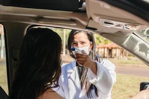 vrouwelijke arts die de temperatuur controleert met behulp van een infraroodthermometer, hulpmiddel voor het detecteren van coronavirus of covid-19, de dame in de auto. foto