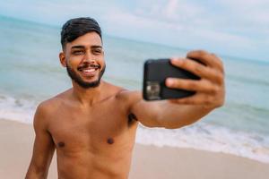 gelukkige Latijns-Amerikaanse man die selfie strandachtergrond, zonnige zomerkleuren maakt. foto