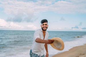 Latijns-Amerikaanse man lacht en gooit zijn hoed en kijkt naar de camera op het strand op een mooie zomerdag foto