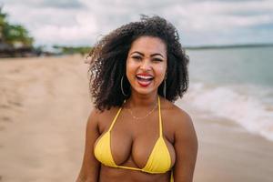 mooie Latijns-Amerikaanse vrouw in bikini op het strand. jonge vrouw geniet van haar zomervakantie op een zonnige dag, glimlachend en kijkend naar de camera foto