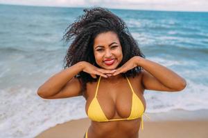 mooie Latijns-Amerikaanse vrouw in bikini op het strand. jonge vrouw geniet van haar zomervakantie op een zonnige dag, glimlachend en kijkend naar de camera foto