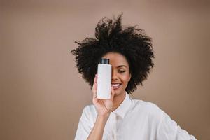 schoonheid latijnse vrouw met afro kapsel. Braziliaanse vrouw. met lege shampooverpakking. gekruld haar. kapsel. pastelkleurige achtergrond. foto