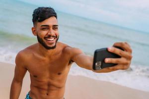 gelukkige Latijns-Amerikaanse man die selfie strandachtergrond, zonnige zomerkleuren maakt. foto