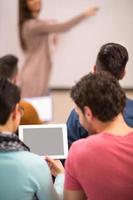 twee studenten kijken naar tablet terwijl professor lezing geeft