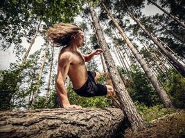 jonge man springen over een boomstam in het bos. foto
