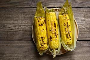 Suikermaïs eten, zoete maïs gekookt op houten plaat achtergrond, rijpe maïskolven gegrilde suikermaïs voor voedsel veganistisch diner of snack - bovenaanzicht foto