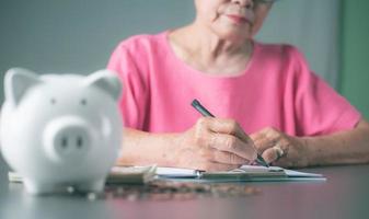 oude senior vrouw zitten en het maken van aantekeningen over haar financiën in een notitieblok. foto