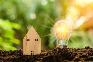 een felle gloeilamp en een gesimuleerd houten huis op de heuvel. het concept voor onroerend goed, economie, financiën, bankieren. dag, natuur, heldere lucht, het licht van de glans in de ochtend. wazig, bokeh achtergrond foto