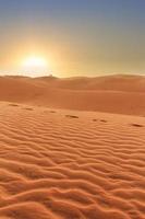 zonsondergang in woestijnlandschap, voetafdrukken in golfde zand