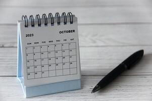 oktober 2023 witte bureaukalender met zwarte pen op houten tafel. foto
