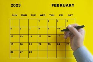 februari 2023 kalender met hand met zwarte pen op gele achtergrond. foto