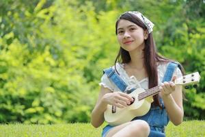 Aziatisch meisje dat ukelele speelt en gelukkig lacht in het park. foto