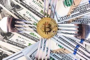 gouden bitcoin op de achtergrond van honderd-dollarbiljetten en bestek. foto