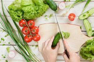 handen die komkommer voor salade op houten achtergrond snijden, hoogste mening foto
