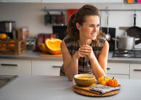 jonge huisvrouw die pompoensoep in keuken eet foto
