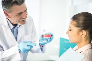 vrolijke tandarts lesgeven op model van menselijke tanden foto